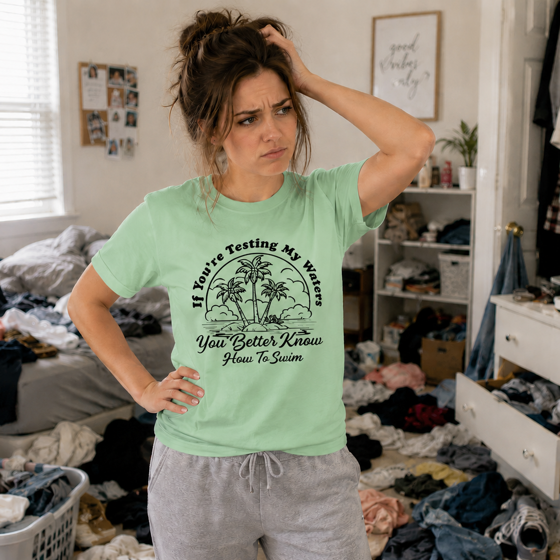 Woman in a messy room wearing a green t-shirt with text and graphics.