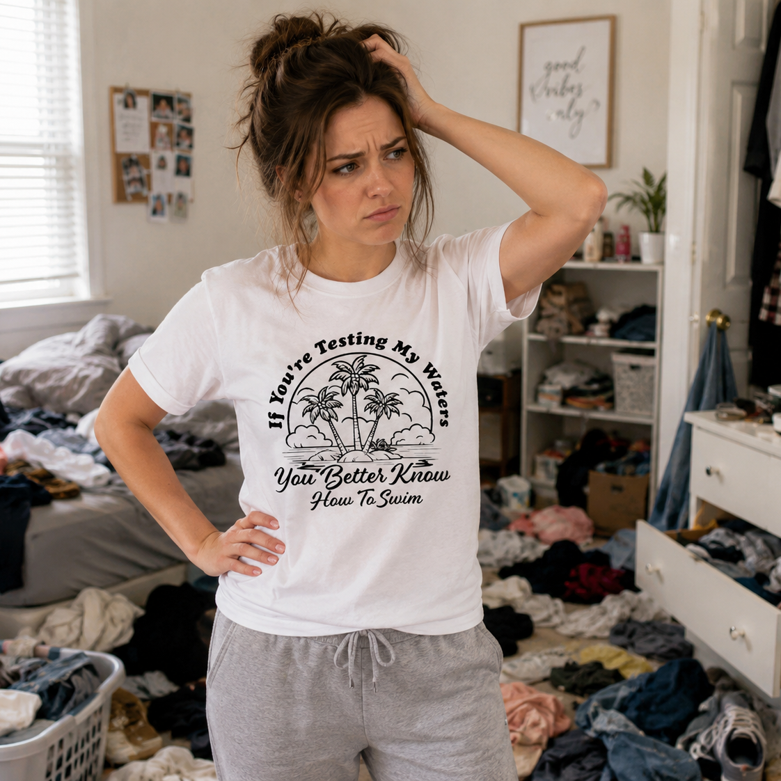 Woman in a messy room wearing a white t-shirt with text and graphics.