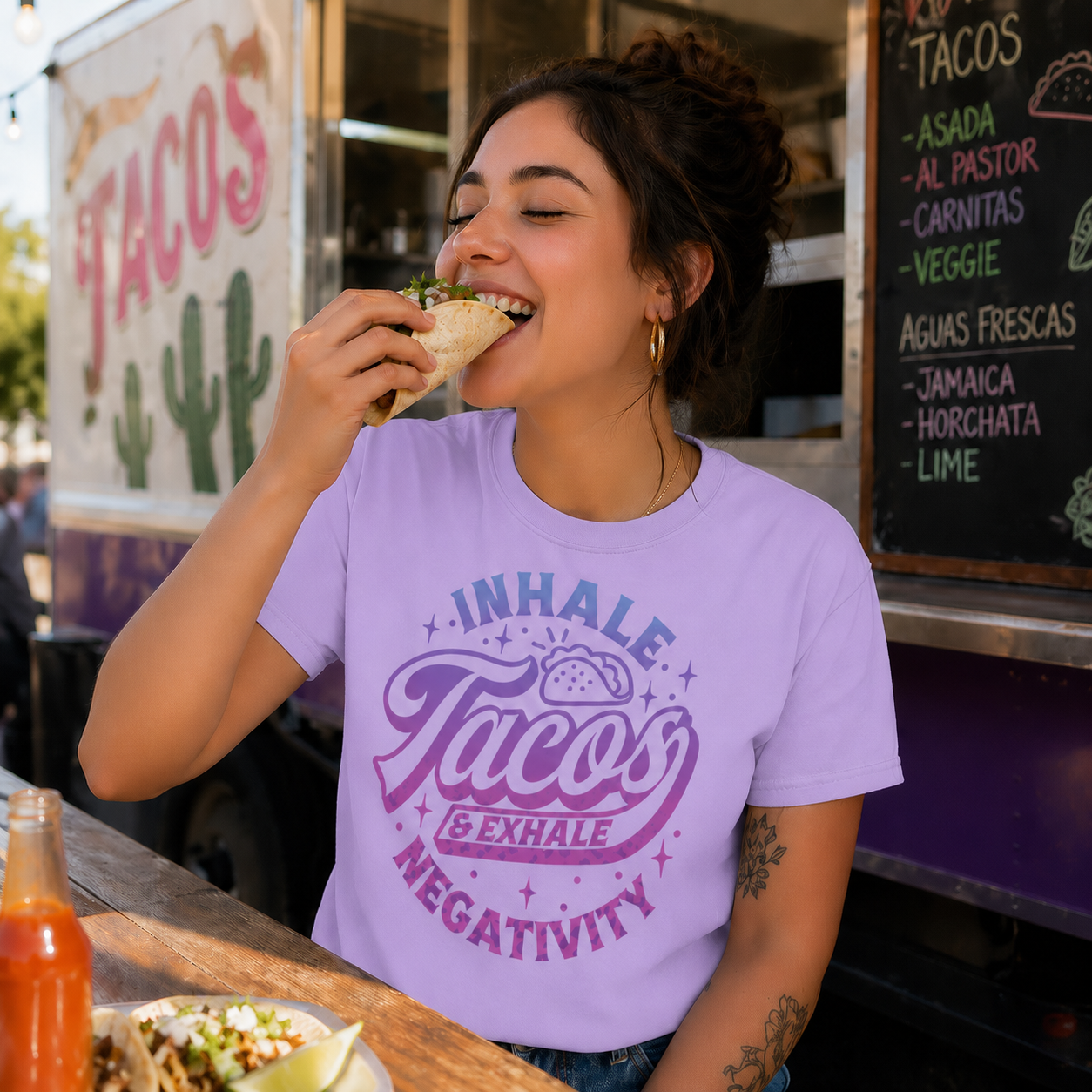 Woman wearing an orchid colored t-shirt with a graphic design with text Inhale Tacos Exhale Negativity