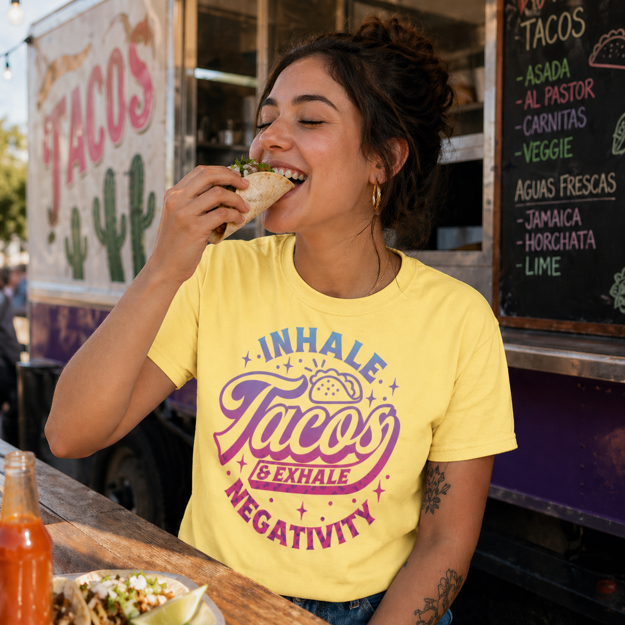 Woman eating a taco in front of a taco truck wearing a yellow t-shirt with a taco-themed message.