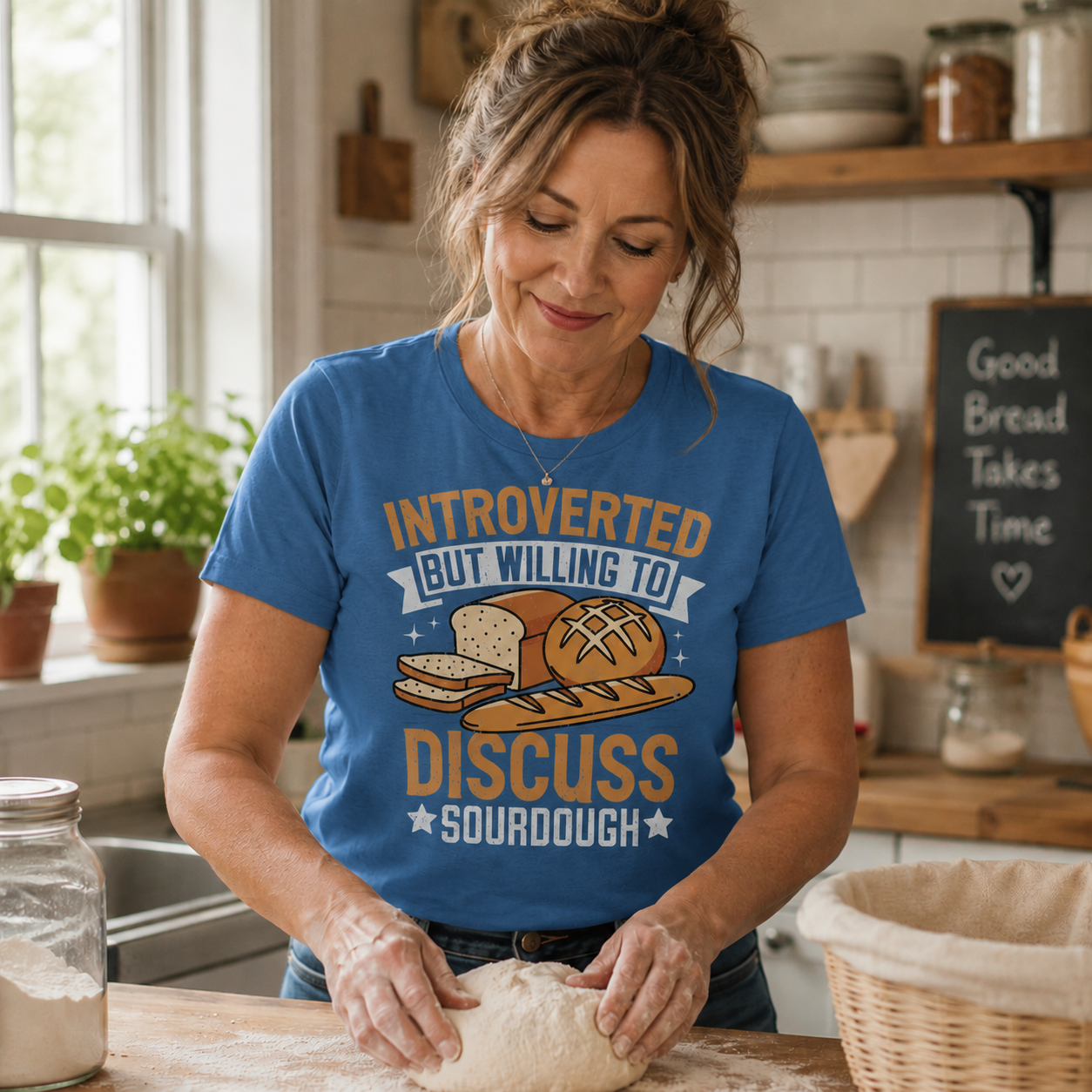 Woman in a kitchen wearing an iris colored t-shirt with bread graphics and text.