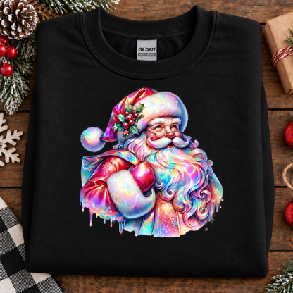 A black Gildan crewneck sweatshirt laid flat on a rustic wooden surface, decorated with Christmas-themed props like pinecones, a gift box, and a plaid cloth. The sweatshirt features a large, vibrant, multicolored graphic of Santa Claus with a rainbow-colored beard, hat, and sack.