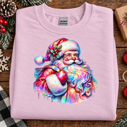 A folded light pink Gildan t-shirt with a colorful, rainbow-iridescent graphic of Santa Claus on the front, displayed on a rustic wooden table with holiday decorations.