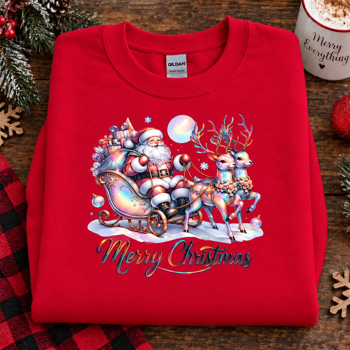 A folded red Gildan sweatshirt with a colorful Christmas graphic of Santa Claus in a sleigh with reindeer and the words 'Merry Christmas' on the front, displayed on a rustic wooden surface with holiday decorations.