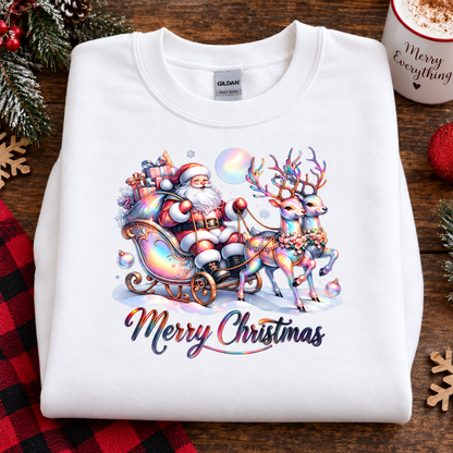 A folded white Gildan sweatshirt with a colorful Christmas graphic of Santa Claus in a sleigh pulled by decorated reindeer, with 'Merry Christmas' text below, displayed on a wooden surface with holiday decorations.