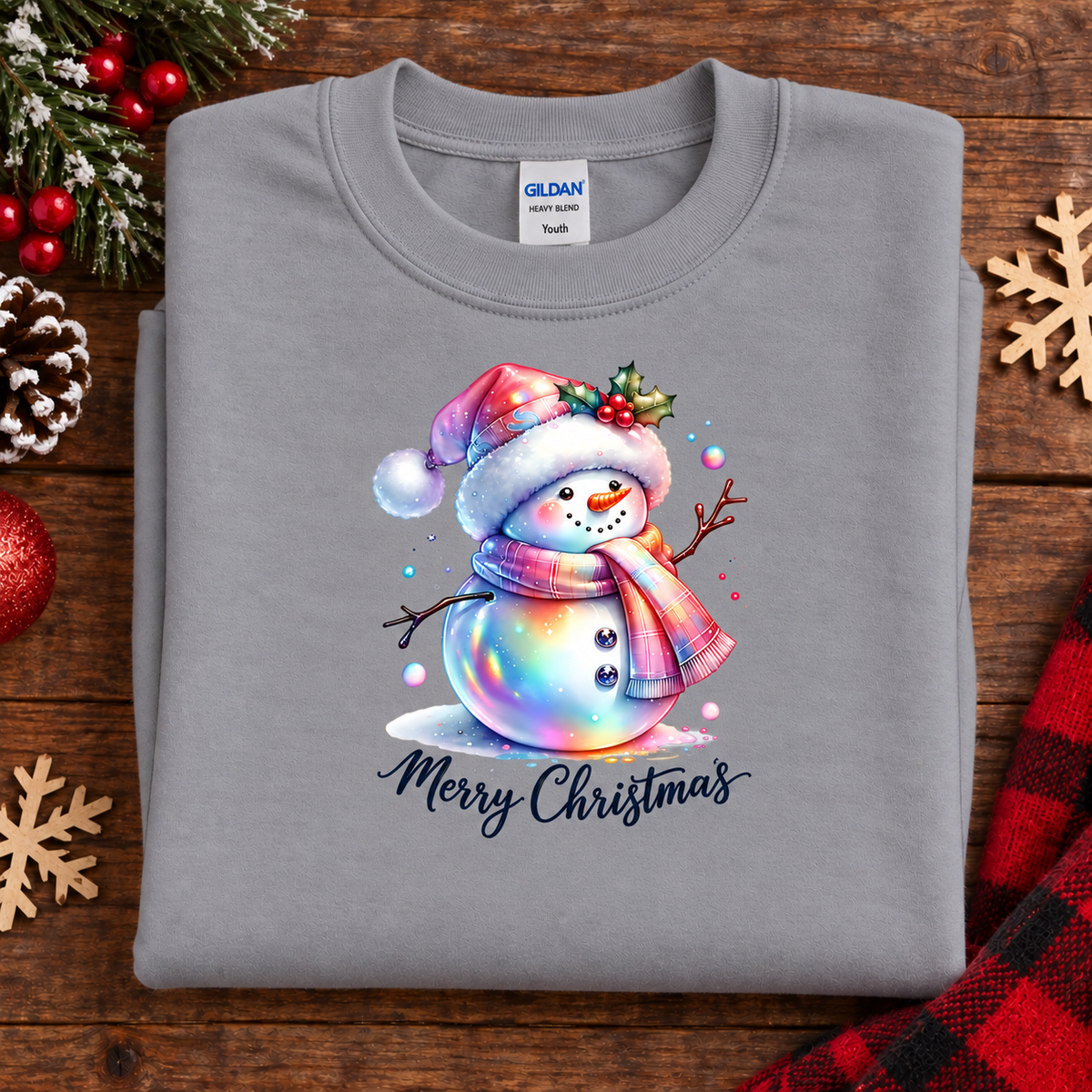 A folded sport gray Gildan Youth crewneck sweatshirt with a colorful Christmas snowman graphic and 'Merry Christmas' text, displayed on a rustic wooden background with holiday decorations.