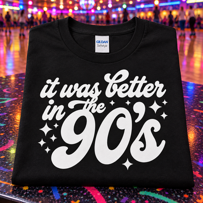 A black Gildan Softstyle t-shirt with a white graphic reading 'it was better in the 90's' and star accents, displayed on a colorful, reflective dance floor with blurred people in the background.