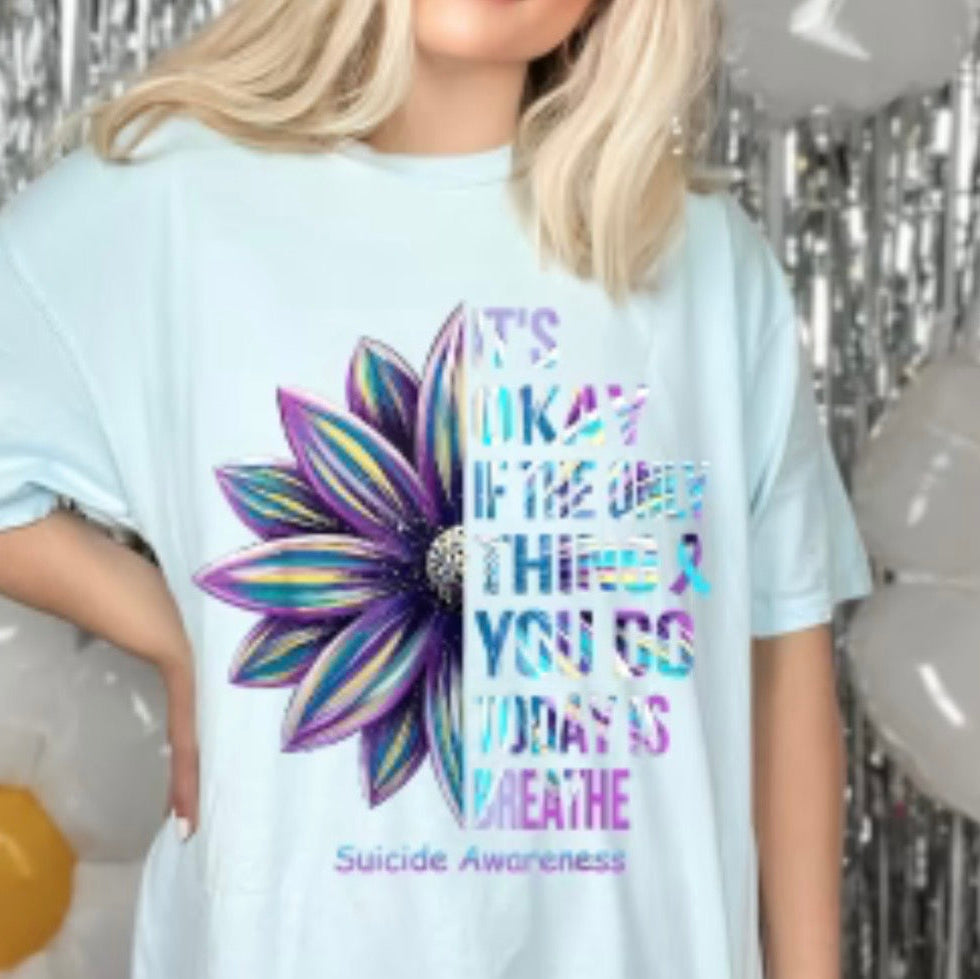 Person wearing a light blue t-shirt with a colorful flower graphic and text about suicide awareness.