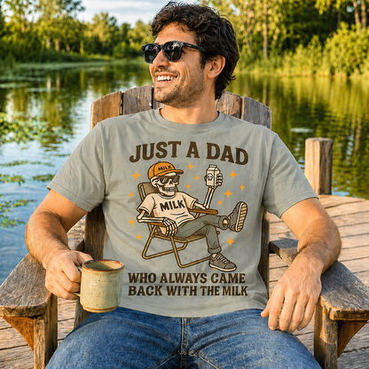 Man wearing a heather military green colored t-shirt with a graphic and text, sitting by a lake.