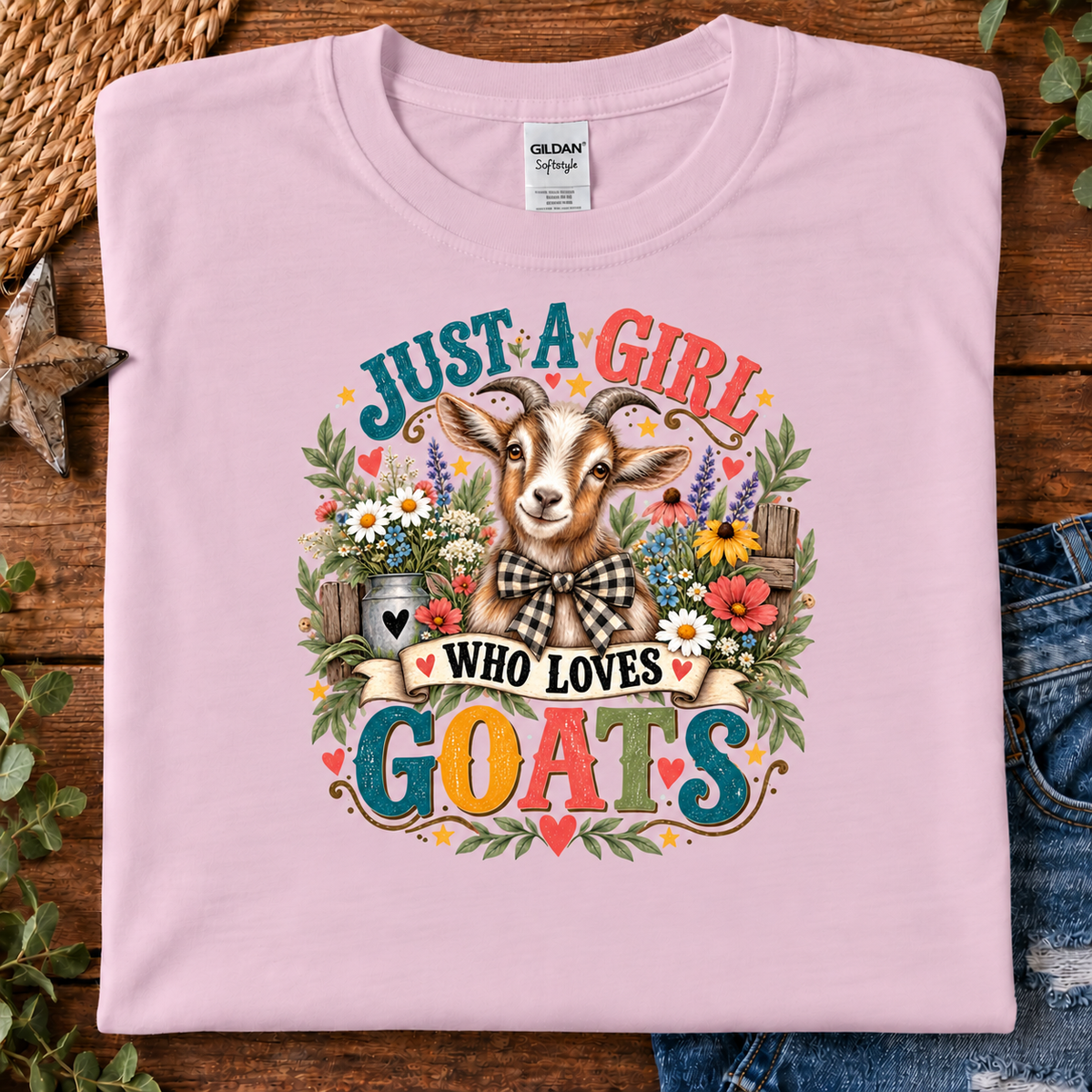 A folded light pink Gildan t-shirt with a colorful graphic of a goat surrounded by flowers and the text 'JUST A GIRL WHO LOVES GOATS'.