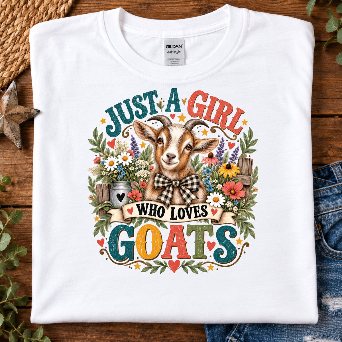 A folded white Gildan t-shirt with a colorful graphic print of a goat surrounded by flowers and the text 'JUST A GIRL WHO LOVES GOATS'.