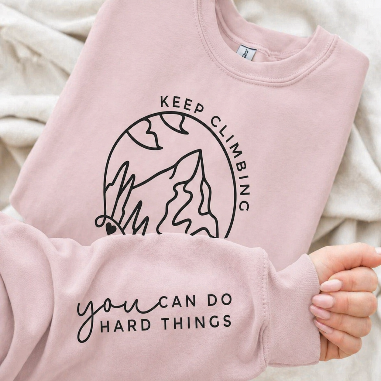 Light pink sweatshirt with motivational text and mountain graphic.