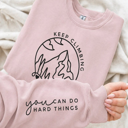Light pink sweatshirt with motivational text and mountain graphic.