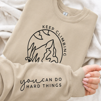 Sand colored sweatshirt with motivational text and mountain graphic on a soft white background