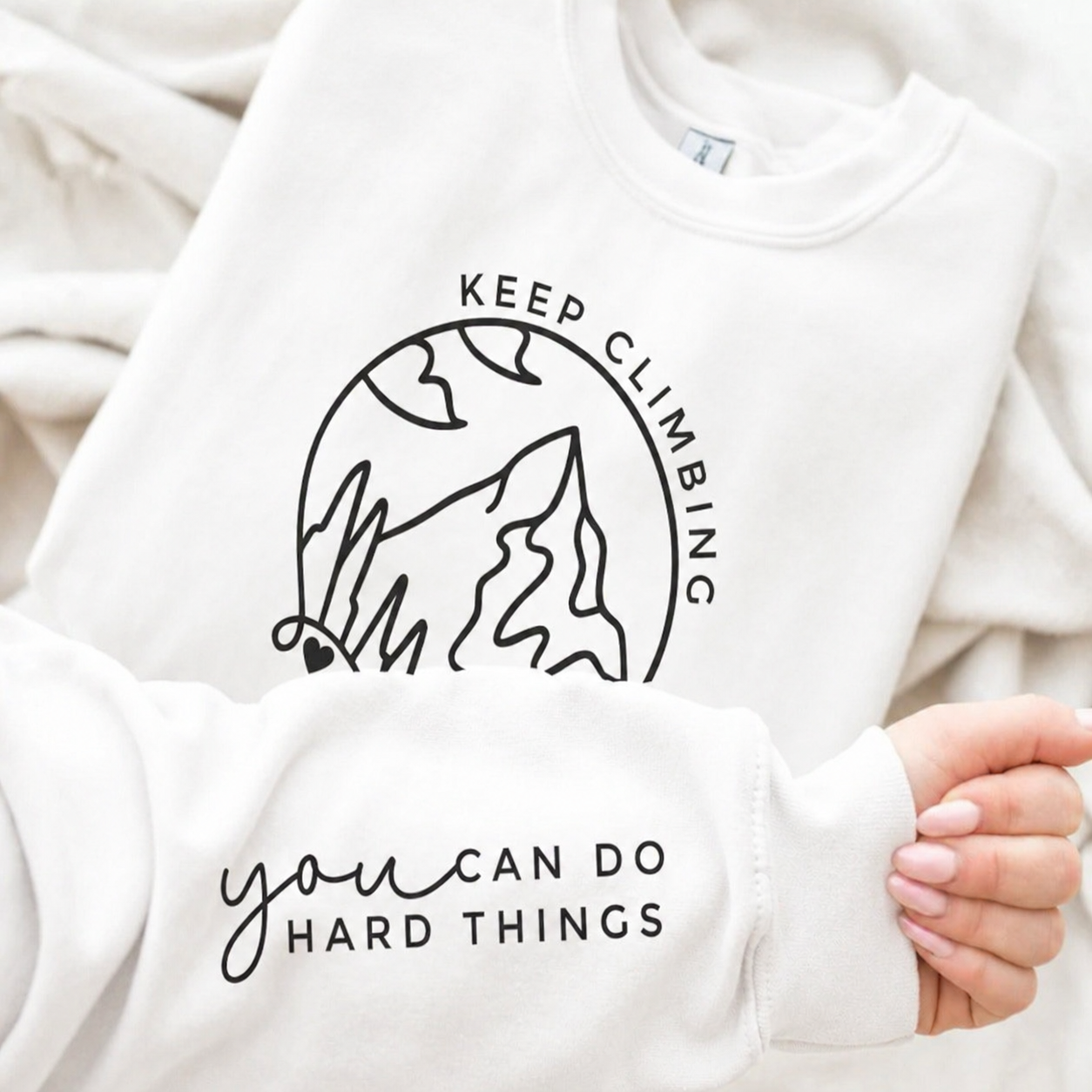 White sweatshirt with motivational text and graphic design held by a person.