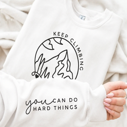 White sweatshirt with motivational text and graphic design held by a person.
