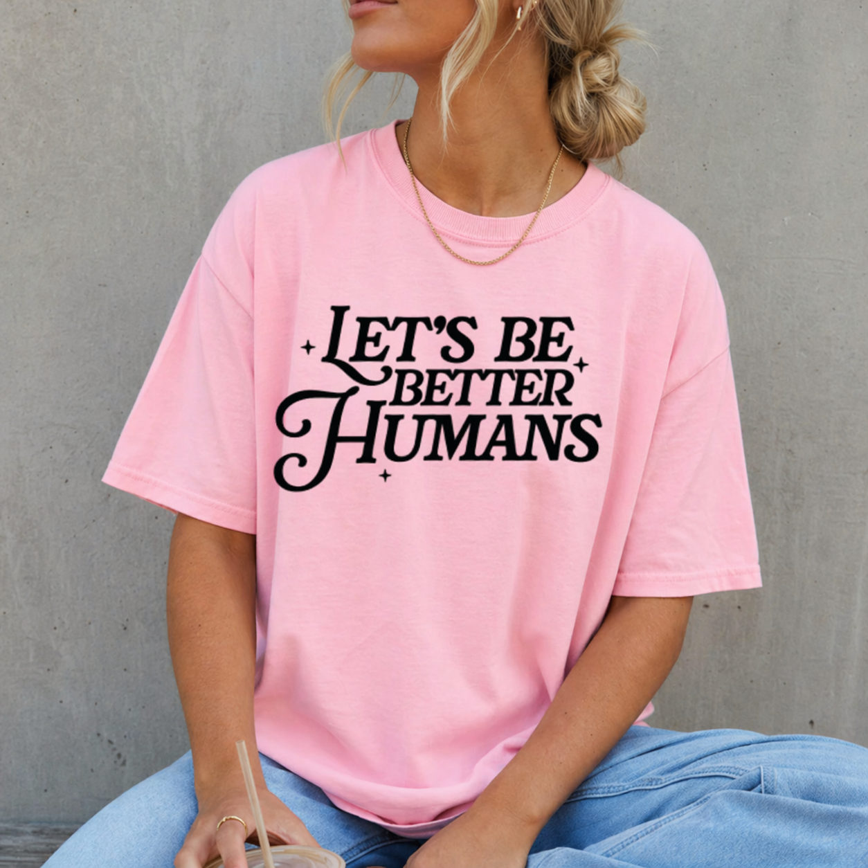 Person wearing a pink t-shirt with 'Let's Be Better Humans' text against a gray background