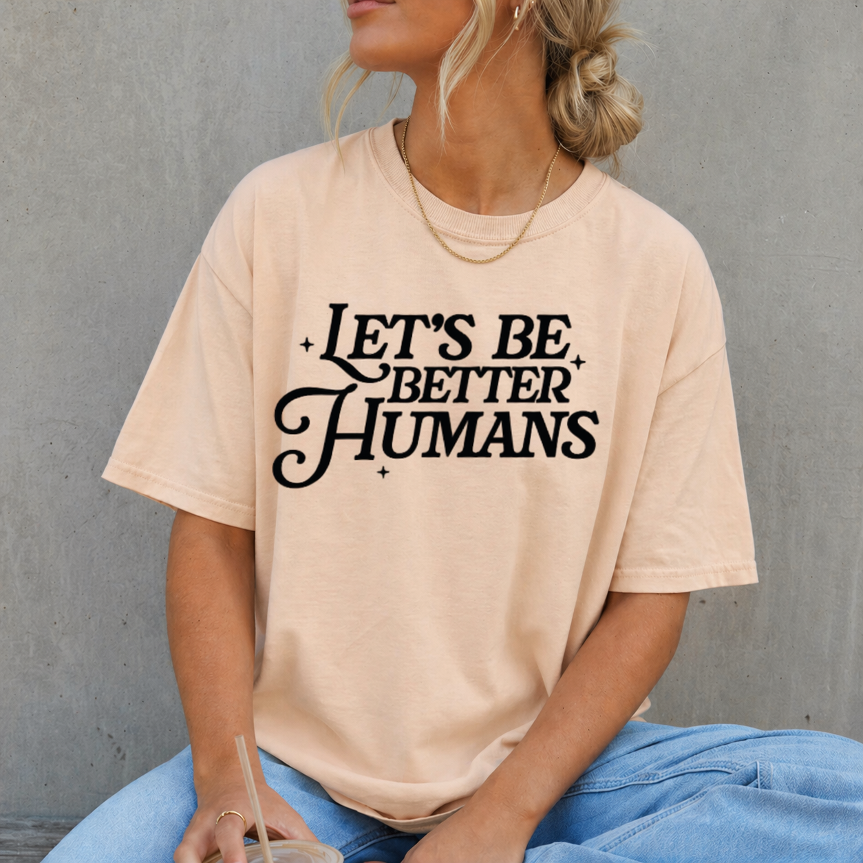 Person wearing a beige t-shirt with 'Let's Be Better Humans' text against a gray background