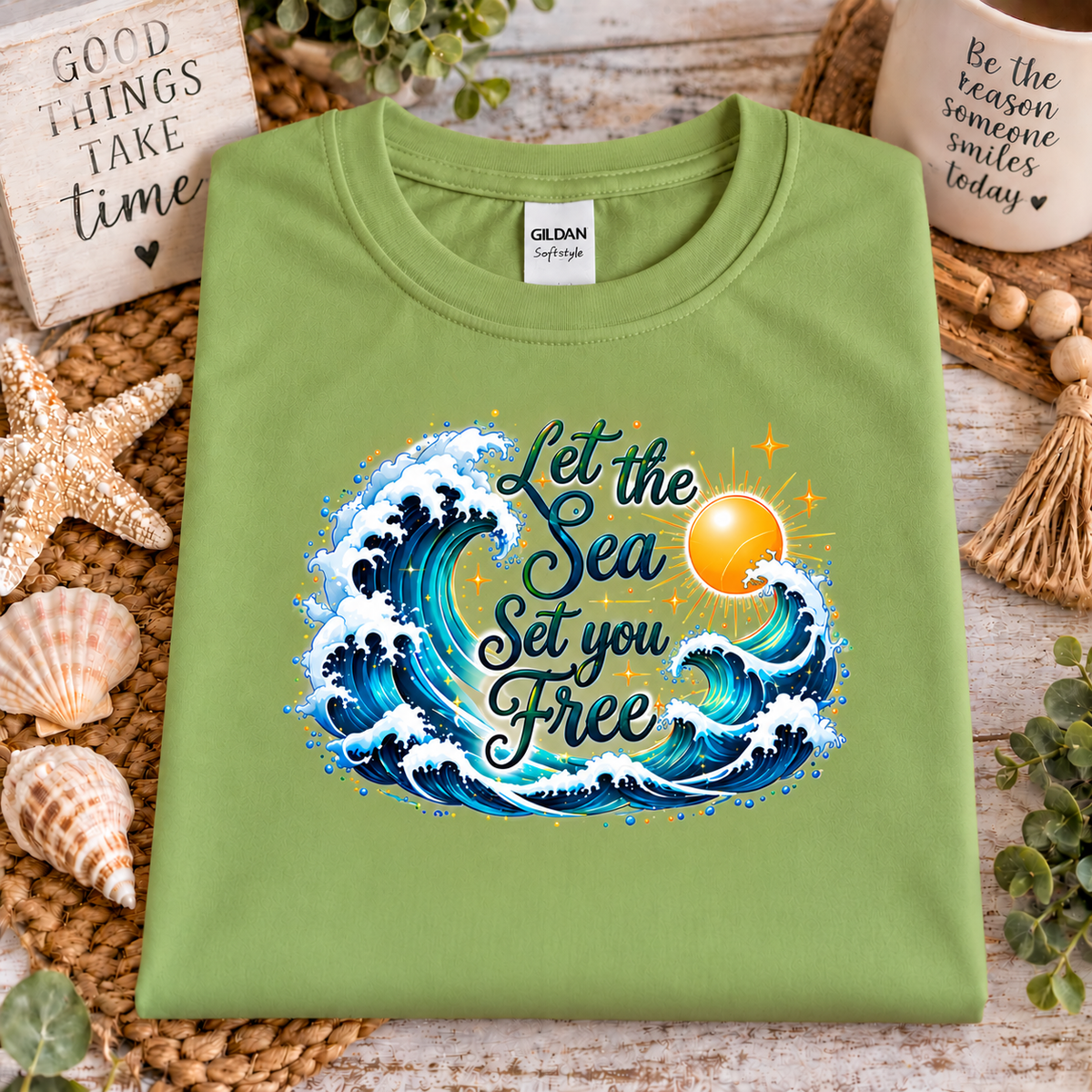 A kiwi green colored gildan softstyle t-shirt with a graphic design with the words "Let the Seas set you free" surrounded by ocean waves and a sun