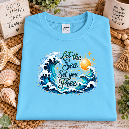 A sky blue gildan softstyle t-shirt with a graphic design with the words "Let the Seas set you free" surrounded by ocean waves and a sun
