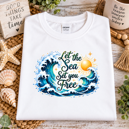 A white gildan softstyle t-shirt with a graphic design with the words "Let the Seas set you free" surrounded by ocean waves and a sun