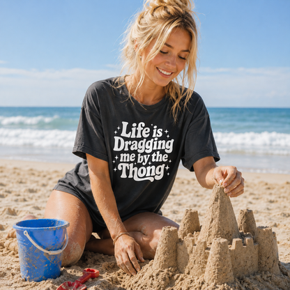 Woman building a sandcastle on the beach wearing a black t-shirt with text.
