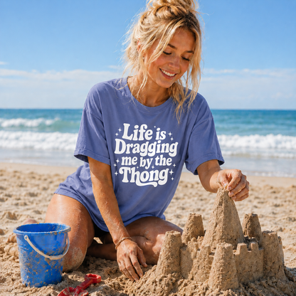 Woman building a sandcastle on the beach wearing a blue t-shirt with text.