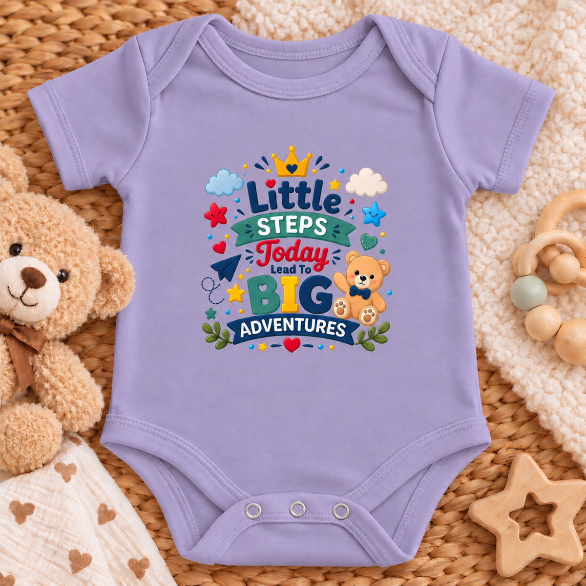 A lavender baby bodysuit with a colorful 'Little Steps Today Lead To Big Adventures' graphic print, styled in a flat-lay with a teddy bear, wooden toys, and a woven mat.