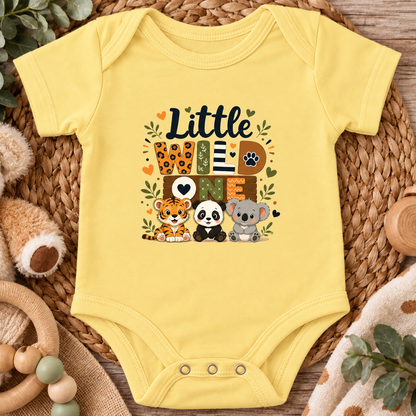 A butter yellow short-sleeve baby bodysuit laid flat on a woven straw mat, featuring a colorful 'Little Love' graphic with cartoon animals including a tiger, panda, koala, and paw print.