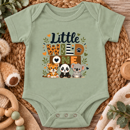 A sage green baby bodysuit with a colorful 'Little Love Wildlife' graphic print, styled flat on a woven straw mat with baby toys and a wooden surface.