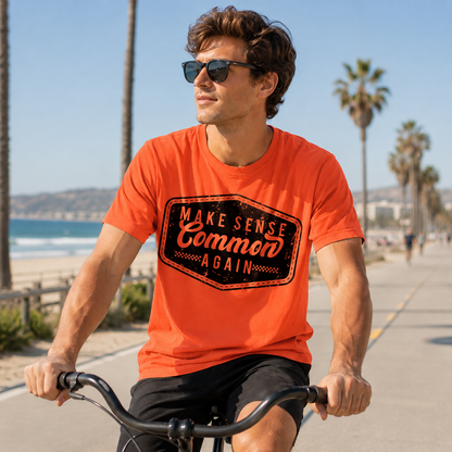 Man riding a bike wearing an orange colored graphic  t-shirt that says Make Sense Common Again