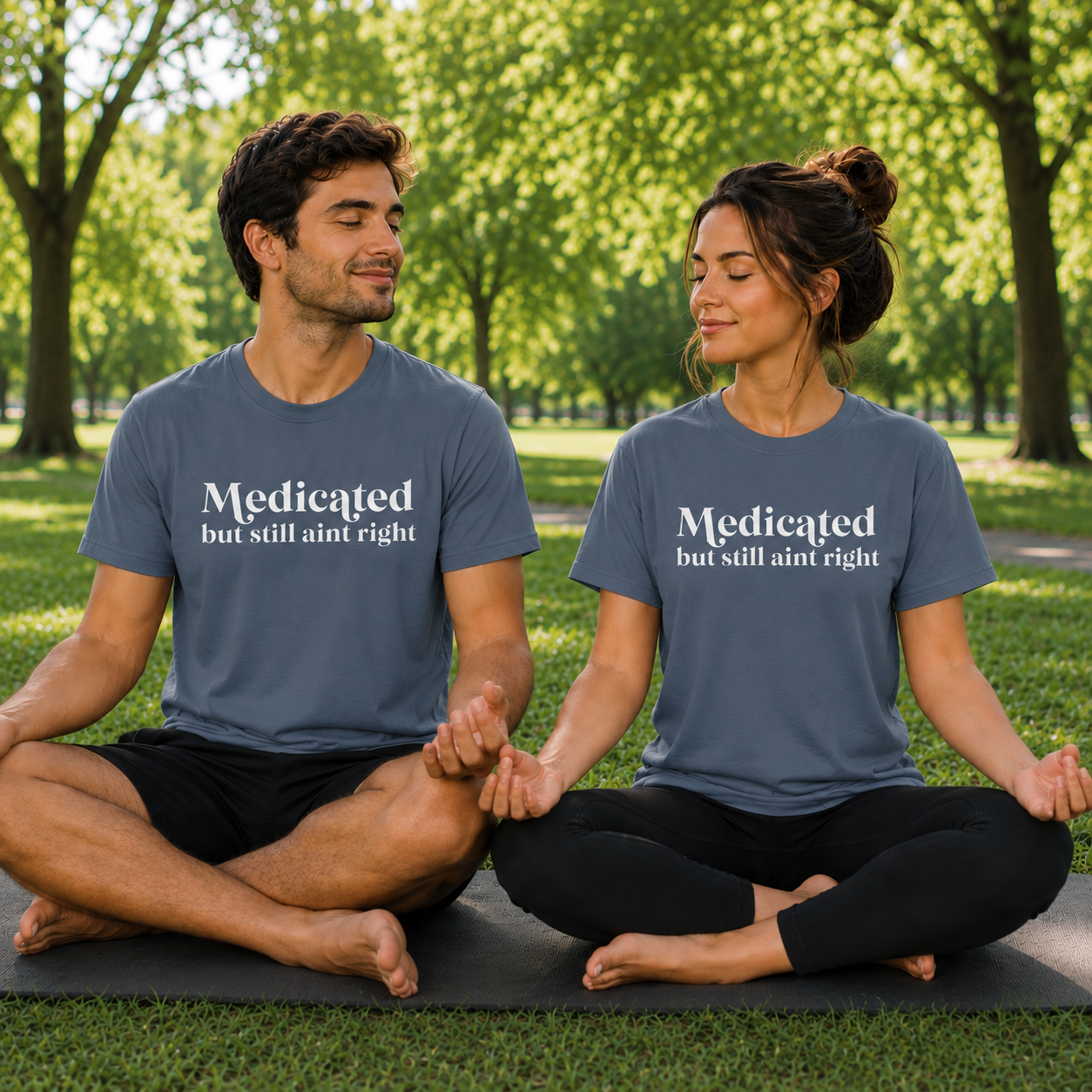 Two people sitting on yoga mats in a park wearing blue jean colored matching t-shirts with text Medicated but still ain't right.