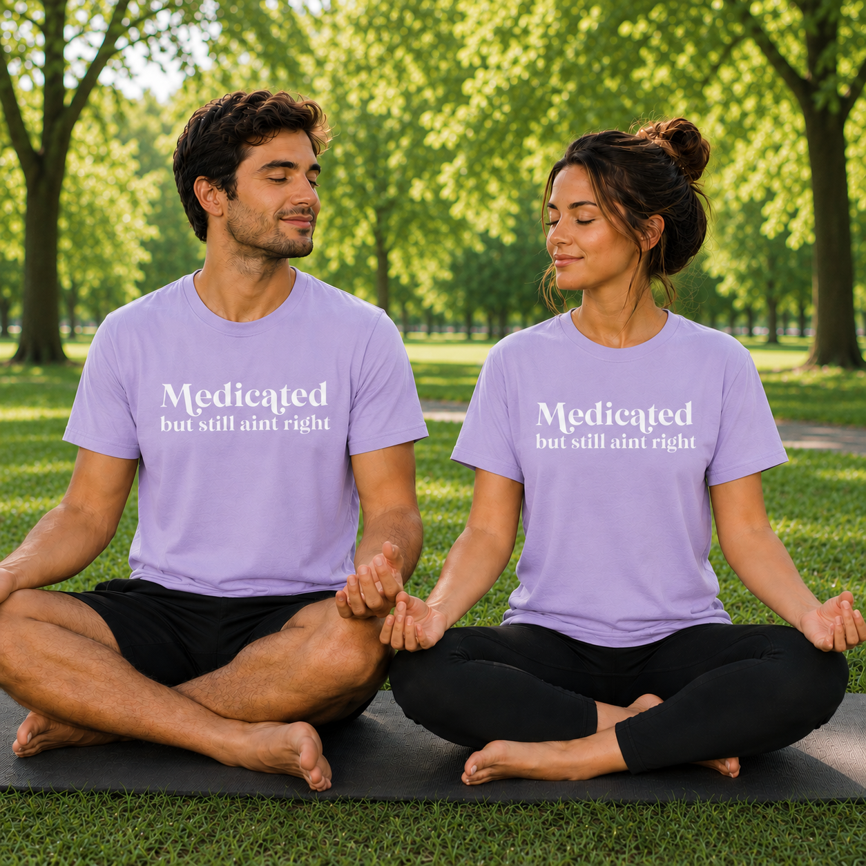 Two people sitting on yoga mats in a park wearing orchid colored matching t-shirts with text Medicated but still ain't right.