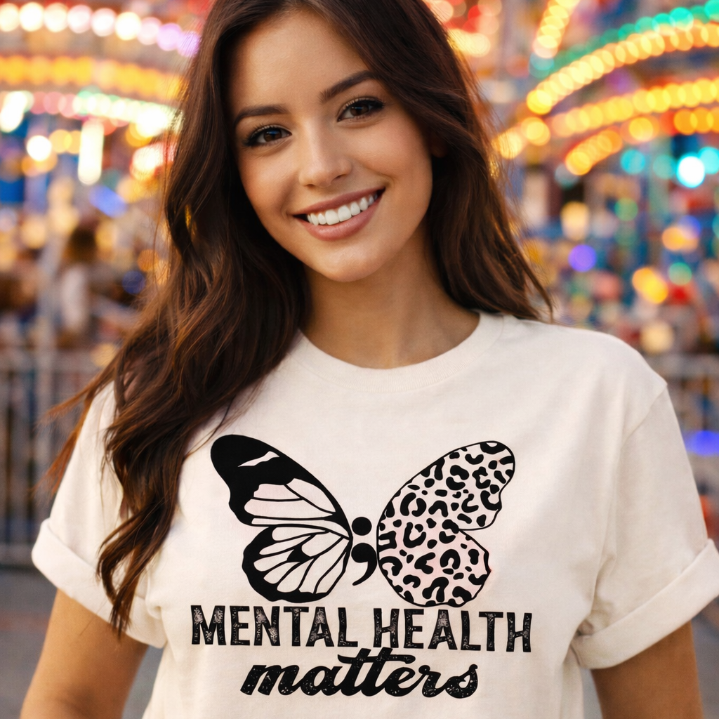 Woman wearing a white t-shirt with a butterfly graphic and 'Mental Health Matters' text at a colorful fairground.