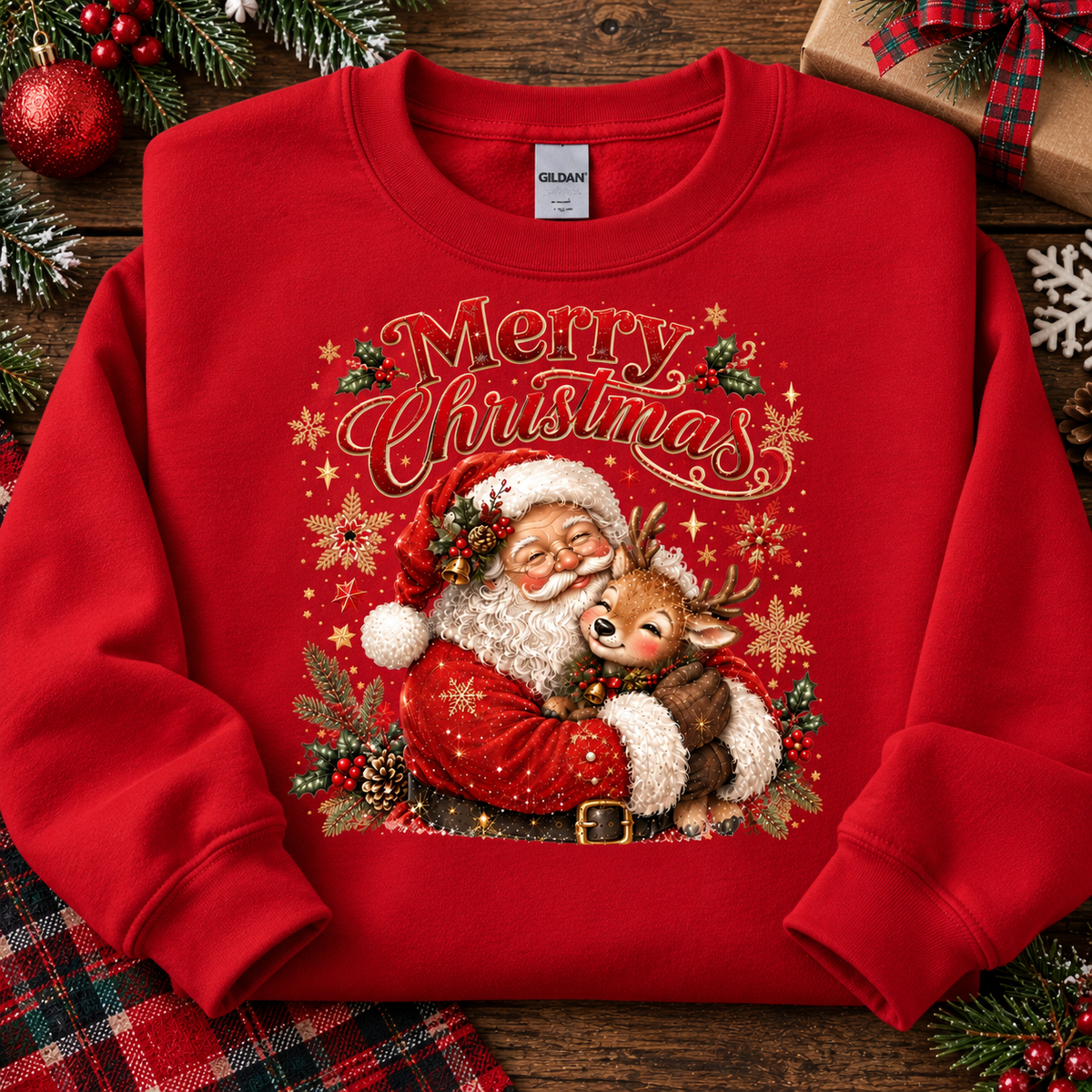 A red crewneck sweatshirt with a large 'Merry Christmas' graphic featuring Santa Claus hugging a reindeer, styled in a flat-lay on a wooden surface with holiday decorations.