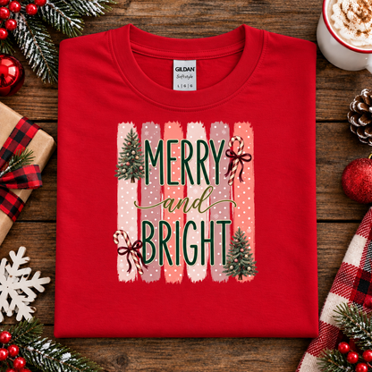 Merry and Bright Christmas graphic on a red t-shirt with striped pink and coral background, white polka dots, green lettering, candy canes with red bows, and two decorated Christmas trees.