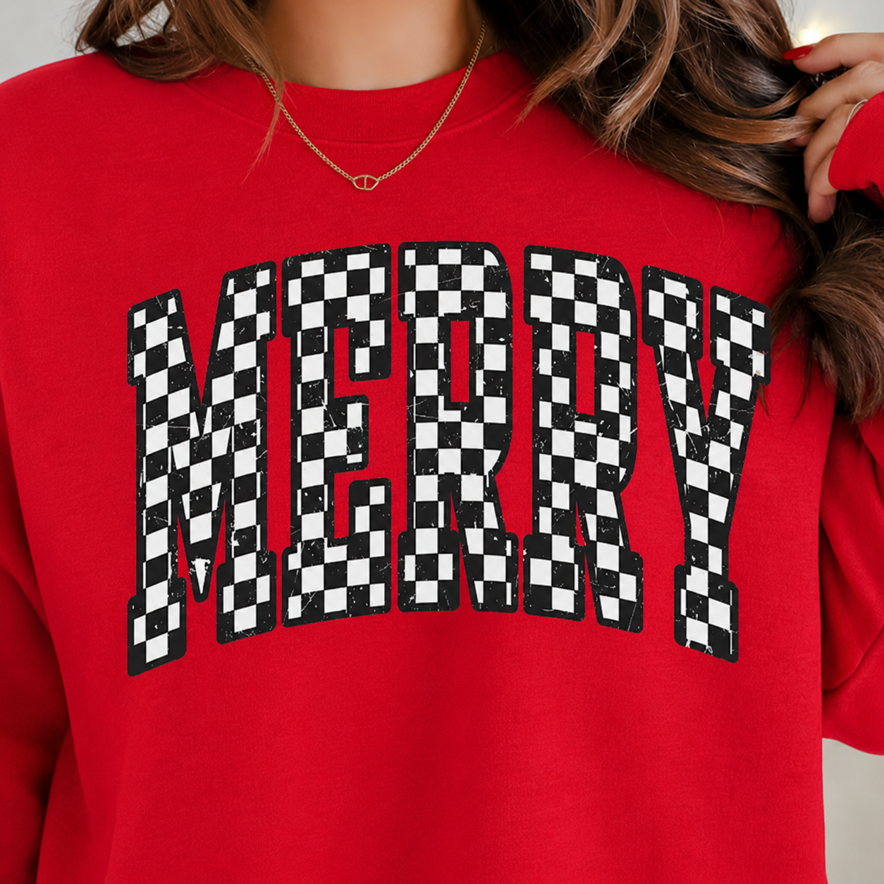 A close-up of a person wearing a bright red sweatshirt with the word "MERRY" in large black-and-white checkerboard letters across the chest.