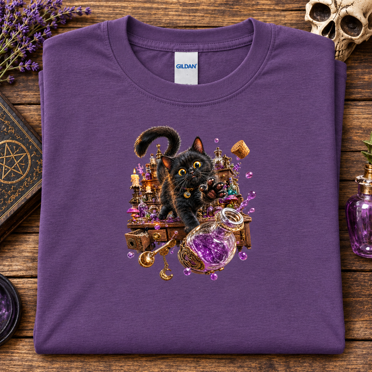A folded heather purple Gildan t-shirt with a detailed graphic of a black cat surrounded by potions and magical items, displayed on a rustic wooden background with occult-themed props.