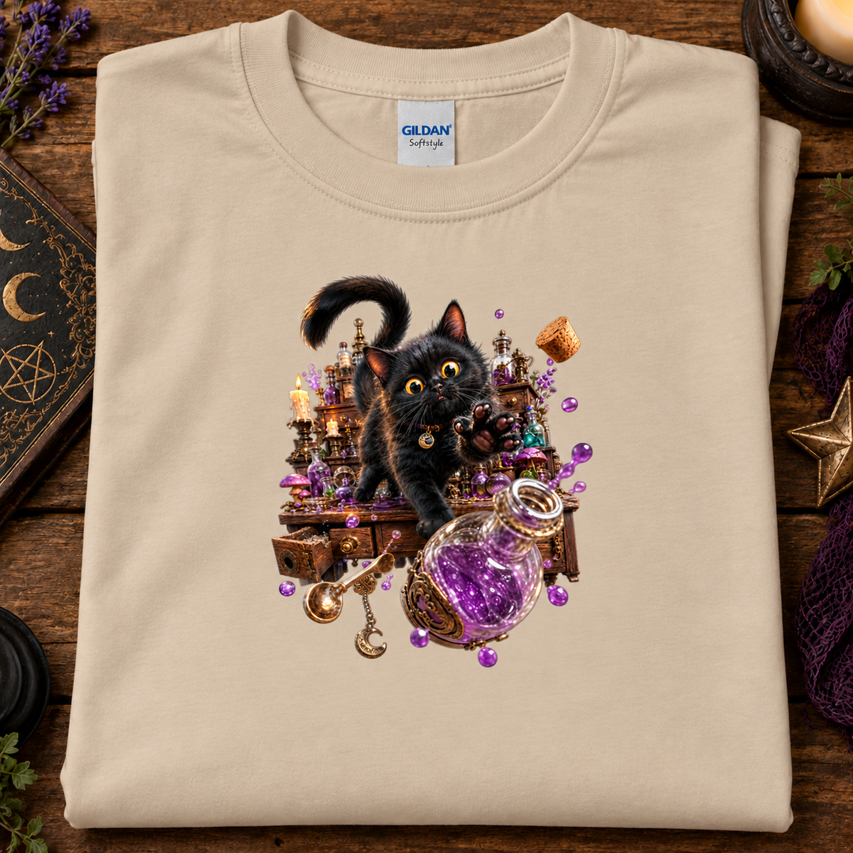 A folded sand crewneck t-shirt by Gildan Softstyle, featuring a detailed graphic of a black cat surrounded by a magical potion bottle, candles, and crystals, displayed on a rustic wooden background.