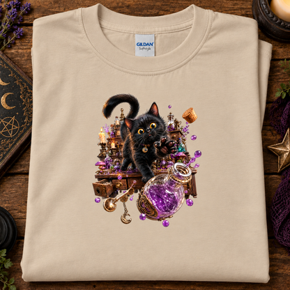 A folded sand crewneck t-shirt by Gildan Softstyle, featuring a detailed graphic of a black cat surrounded by a magical potion bottle, candles, and crystals, displayed on a rustic wooden background.
