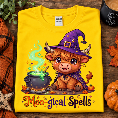 A folded daisy yellow Gildan Comfort T-shirt with a colorful cartoon graphic of a fluffy brown creature wearing a purple witch hat and cape beside a cauldron, with the text 'Moo-gical Spells' below. The shirt is styled on a rustic wood surface with autumn leaves, a candle, and a small pumpkin.