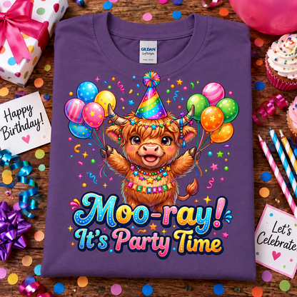 A folded heather purple Gildan Comfort T-shirt with a colorful cartoon Highland cow birthday graphic and the text 'Moo-ray! It's Party Time,' styled on a wooden surface with confetti, cupcakes, balloons, and birthday decorations.