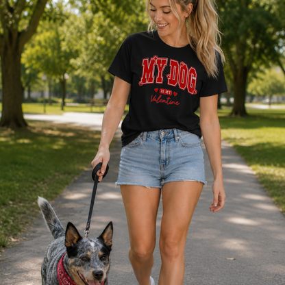 Woman walking a dog on a leash in a park wearing a black t-shirt with red text and denim shorts.