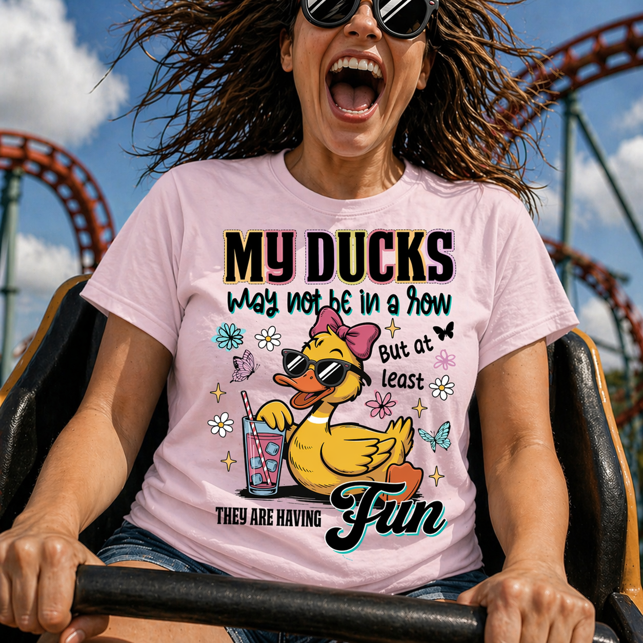 Person wearing a pink t-shirt with a duck graphic and text at an amusement park.