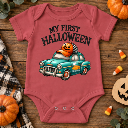 A vintage red baby bodysuit with a 'My First Halloween' graphic featuring a teal car and a jack-o'-lantern, styled in a flat lay on a rustic wooden background with candy corn, pumpkins, and a plaid blanket.
