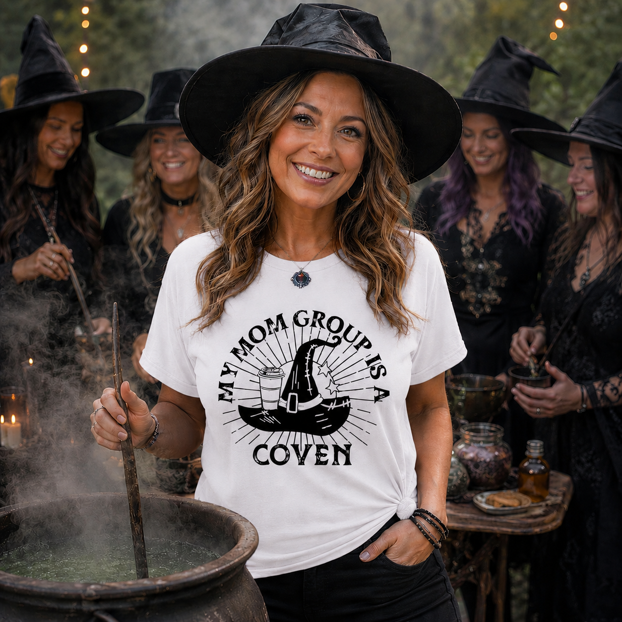 Woman wearing a white t-shirt with a witch hat graphic and text, standing in front of a group of people in witch costumes.