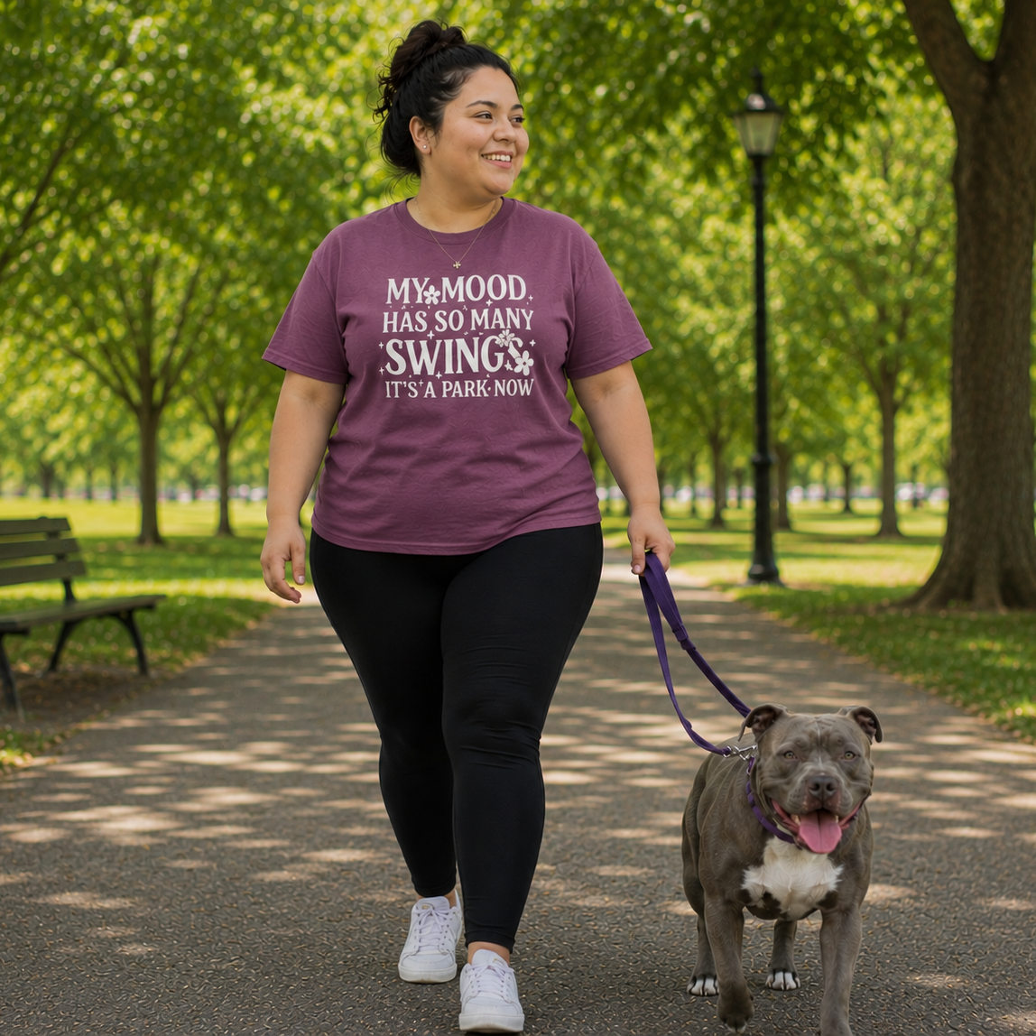 Woman walking a dog in a park wearing a berry colored t-shirt with text.