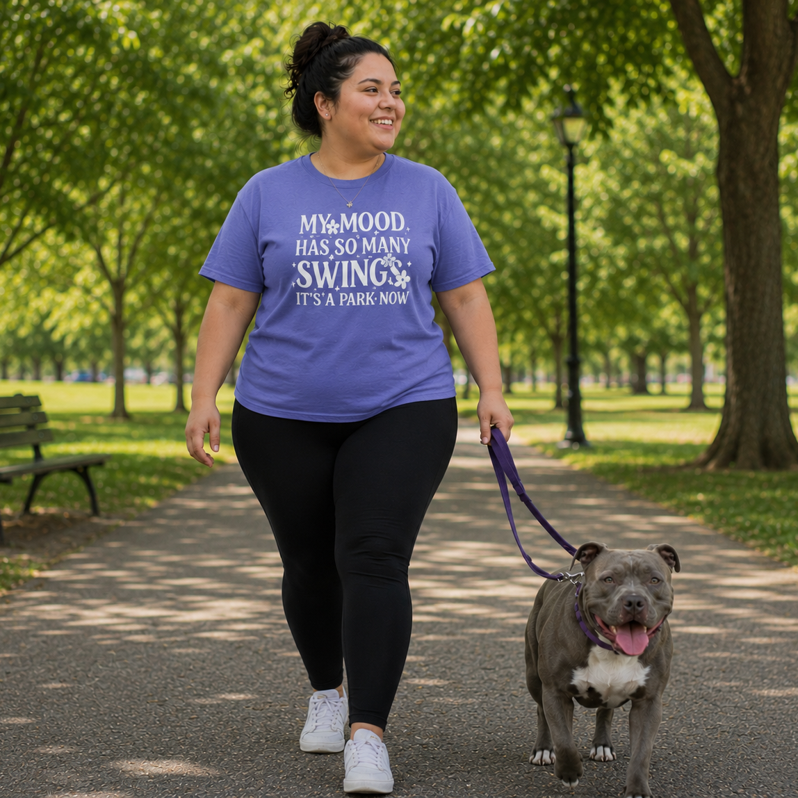 Woman walking a dog in a park wearing a purple t-shirt with text.