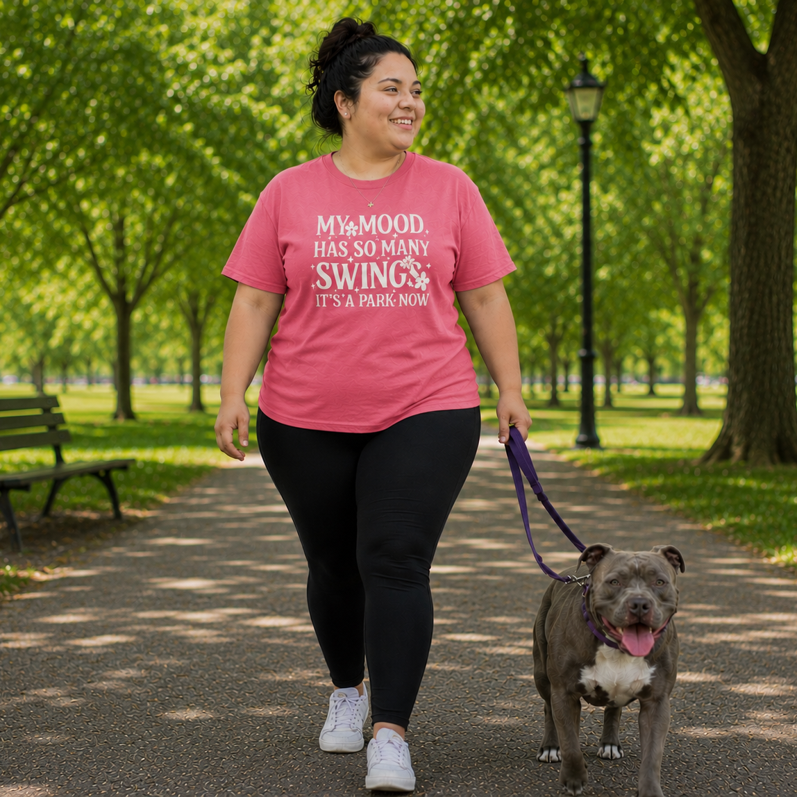 Person walking a dog in a park wearing a pink t-shirt with text.