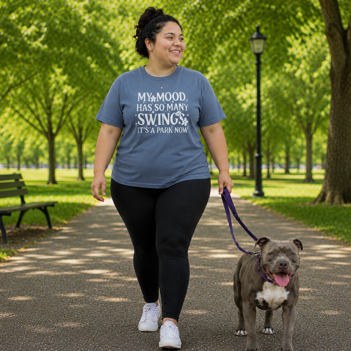 Person walking a dog in a park wearing a blue jean colored t-shirt with text.